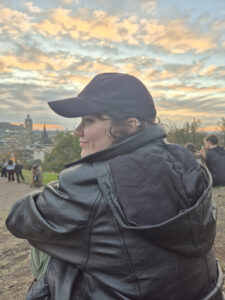 Eine Person mit Cape von hinten mit Gesicht seitlich nach links gewandt, leicht lächelnd