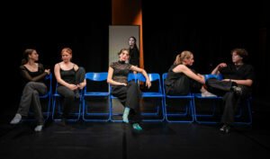 mehrere Personen sitzen auf blauen Stühlen