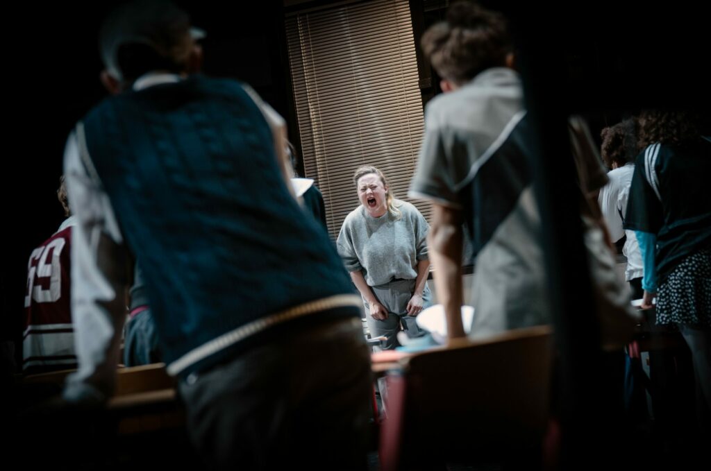 Eine Person schreiend zwischen den Rücken zweier uns weggewandter Personen im Hintergrund zu sehen