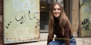 Eine Person, sitzend rechts mit Armen unter den Beinen, lächelnd