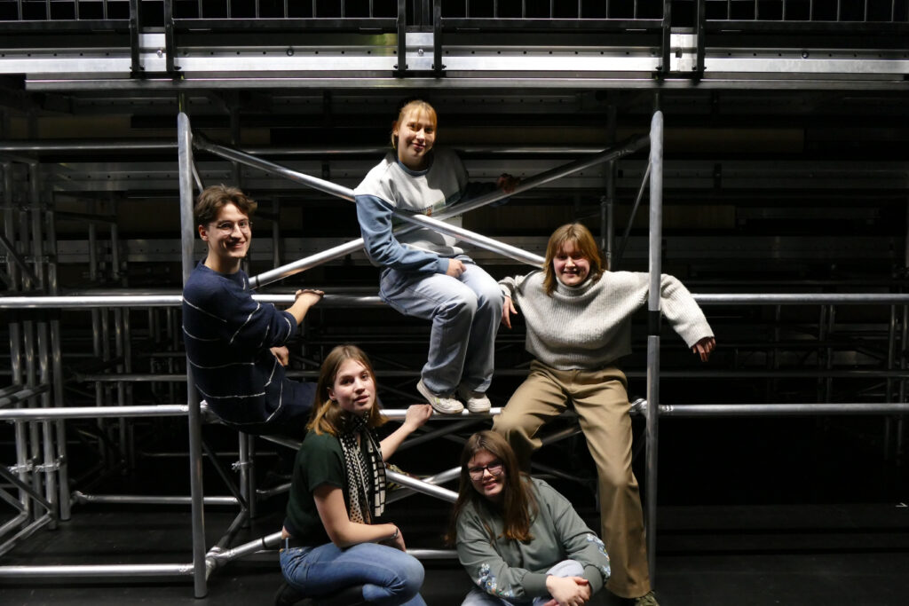 Eine Gruppe fünf junger Menschen, die in einem Bühnengerüst posieren