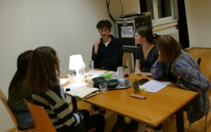 mehrere Personen sitzen um einen Tisch, wirken ins Gespräch versunken