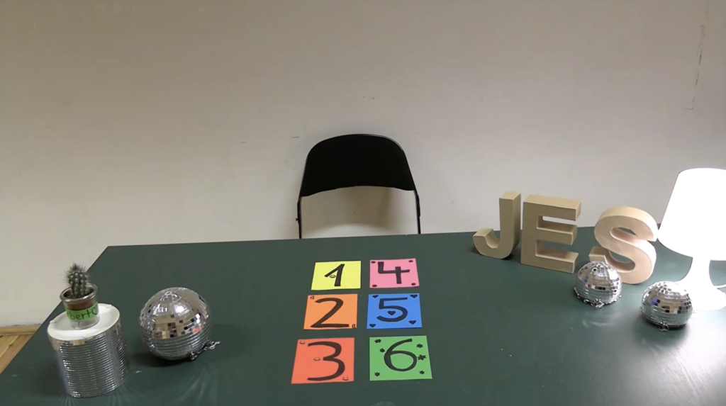 Auf einem Tisch liegen bunt hinterlegte Zahlen, hinter dem Tisch steht ein Stuhl