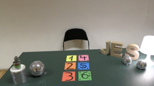 Auf einem Tisch liegen bunt hinterlegte Zahlen, hinter dem Tisch steht ein Stuhl